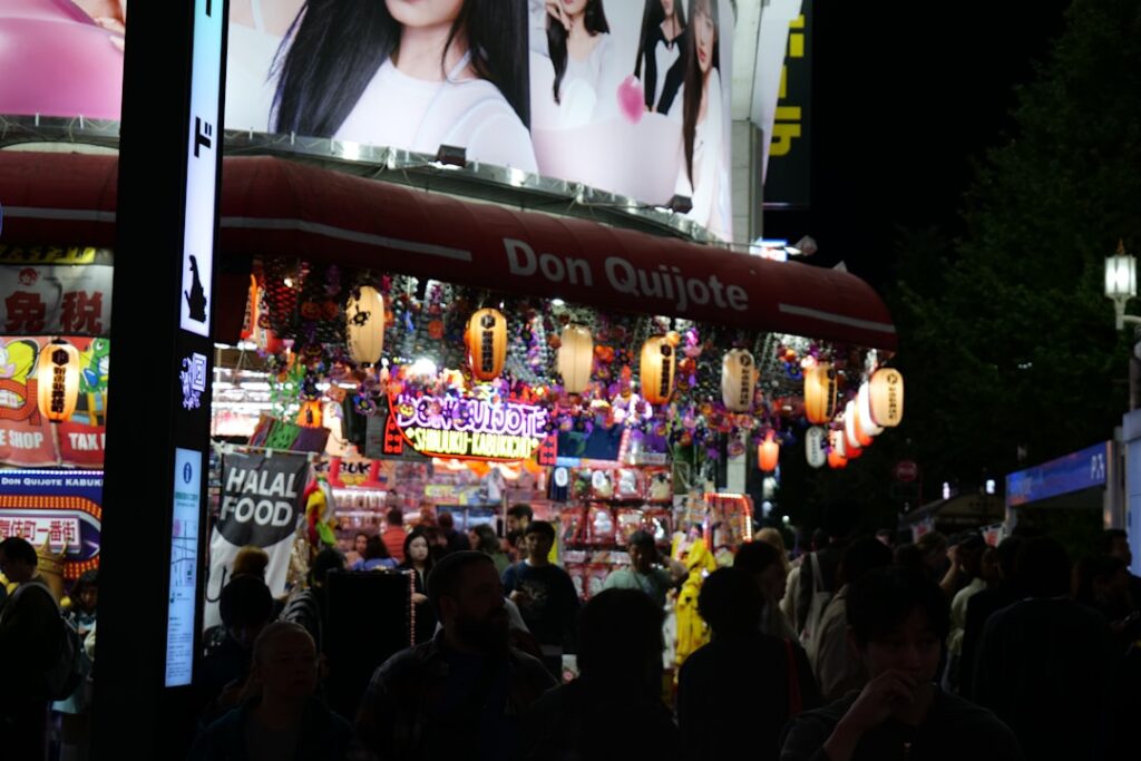 Crowded street market at night with bright signs.