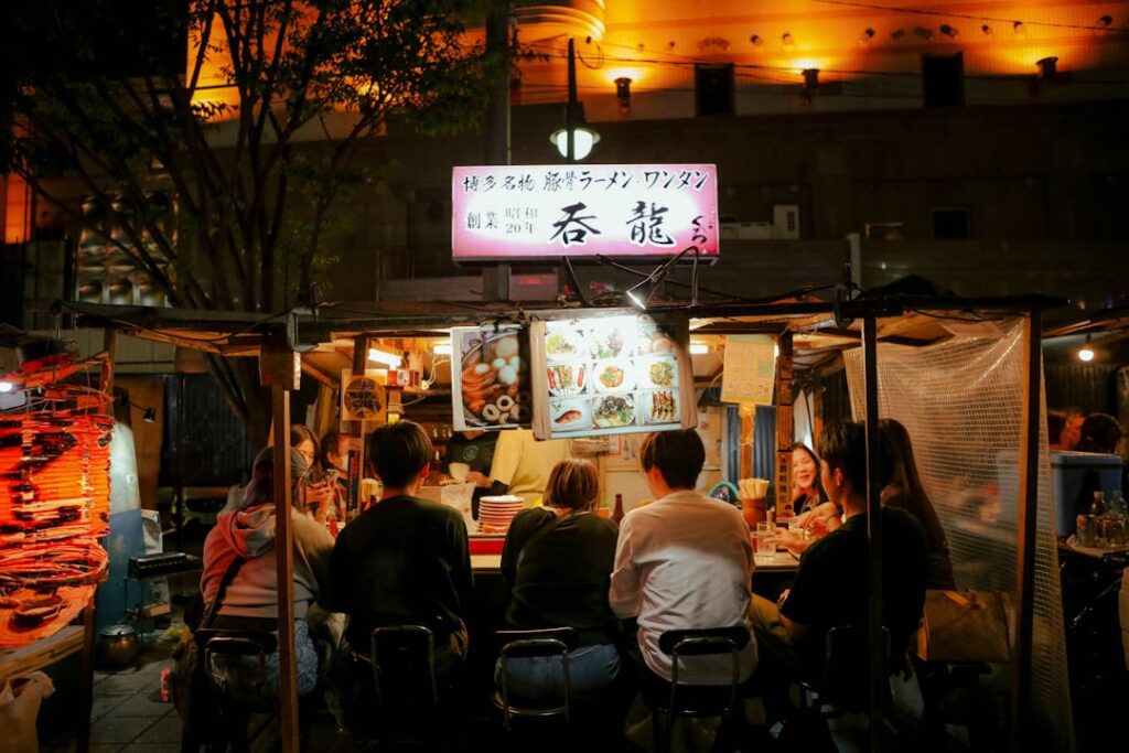 People eat at an outdoor ramen restaurant at night.